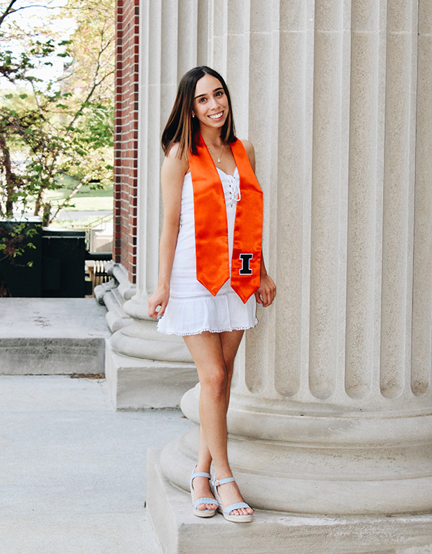 Smiling young woman in white dress and orange graduation stole 