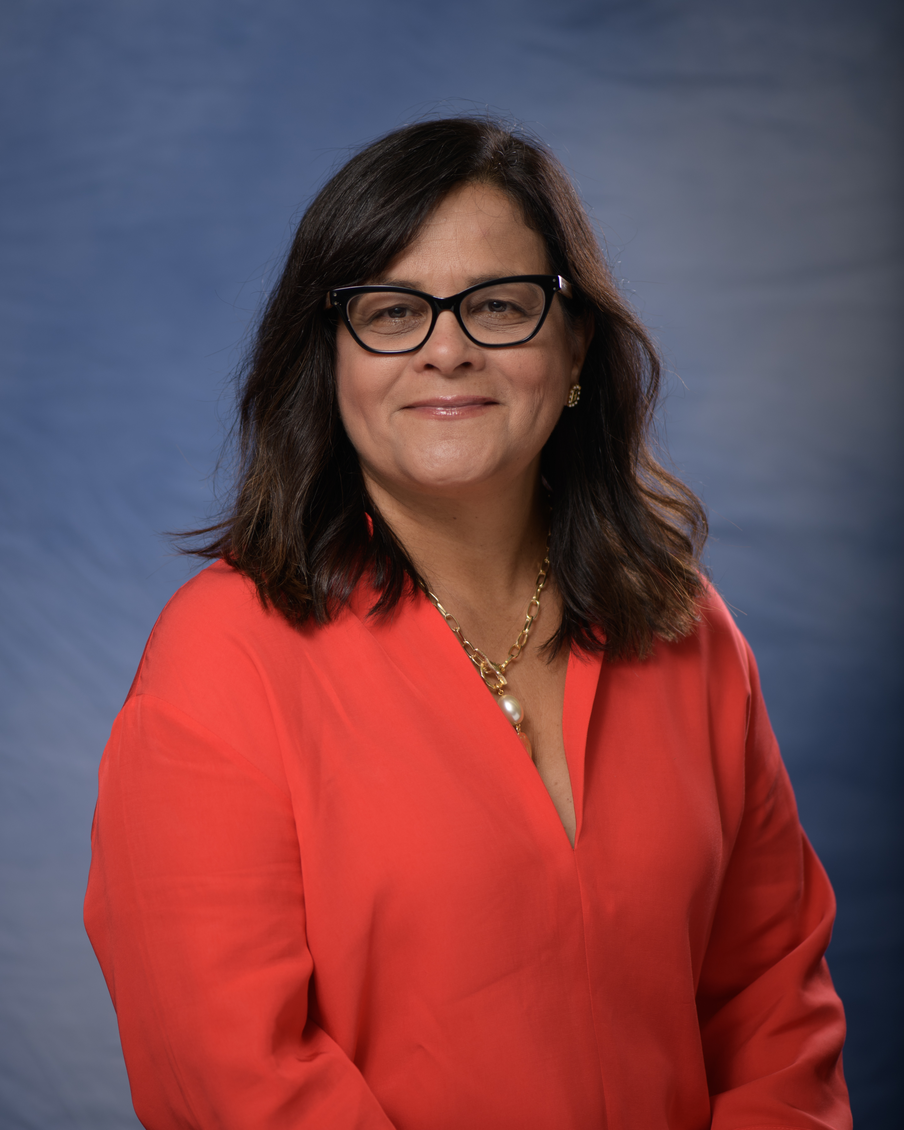 Headshot of smiling woman with dark hair, glasses, and bright orange shirt