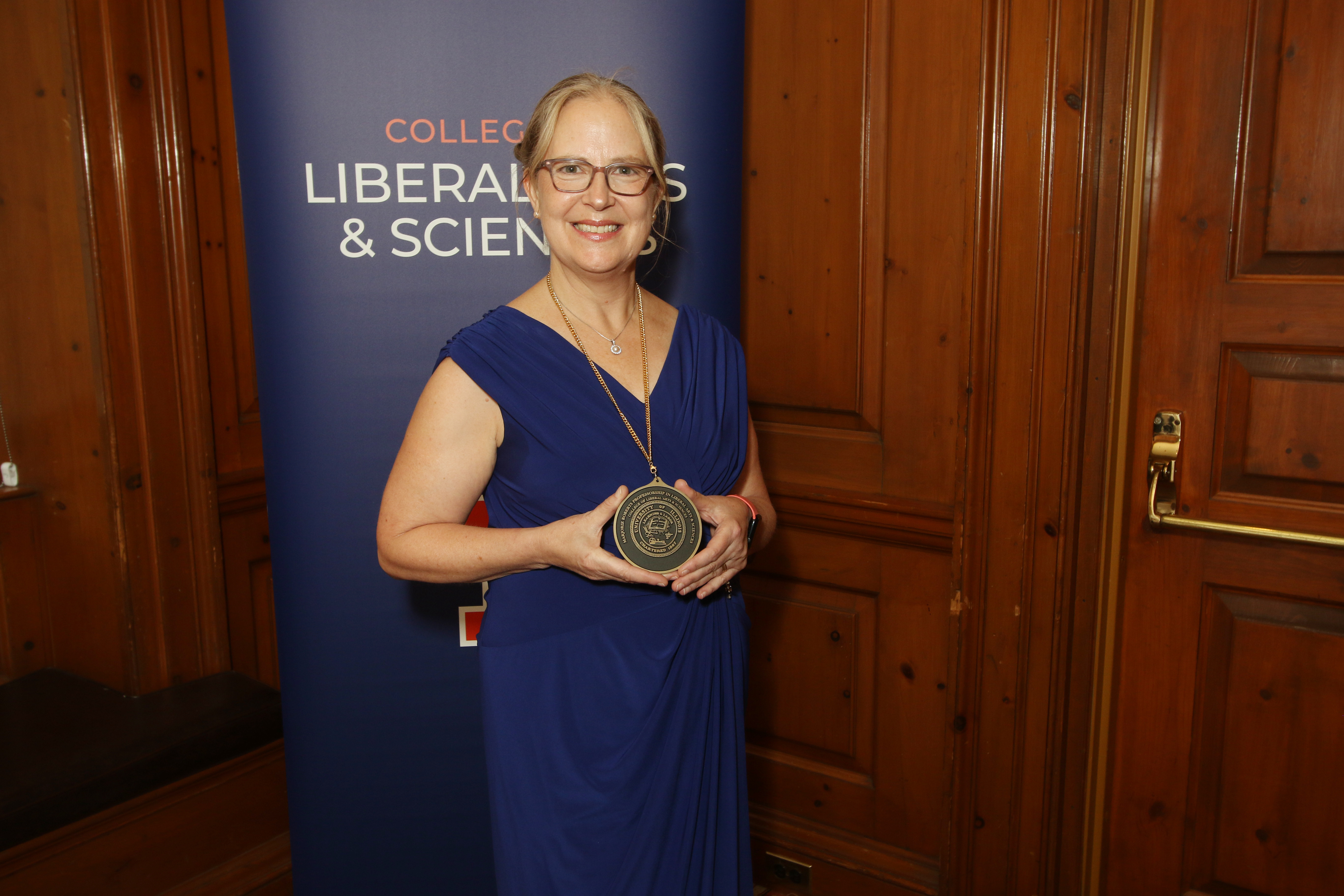 Woman in formal blue dress poses with medallion