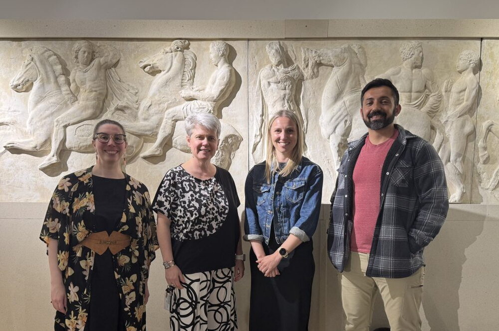 Four people stand in front of classical art display