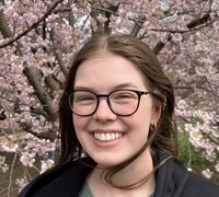 Smiling woman in glasses poses in front of cherry blossom tree