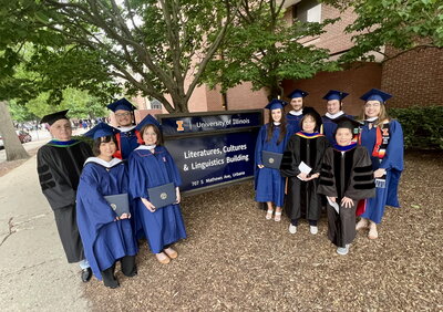 Group of graduates surrounds Literatures, Cultures & Linguistics Building sign