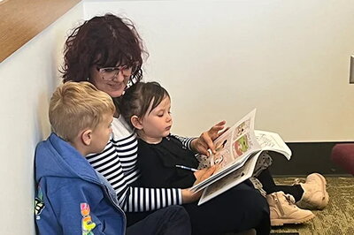 Woman sitting on floor, reading book to two children.