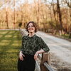 Woman leans on fence with woods behind her 