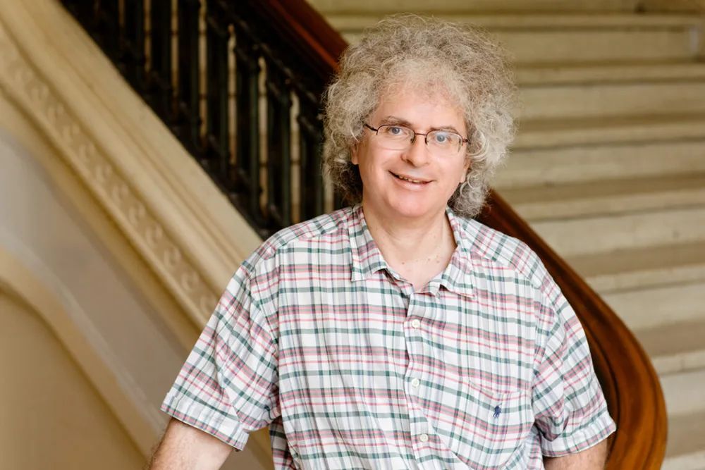 Man in short-sleeve button down and glasses stands by stairs
