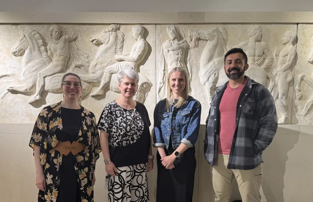 Four people stand in front of classical art display