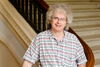 Man in short-sleeve button down and glasses stands by stairs