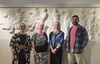 Four people stand in front of classical art display