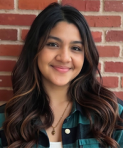 Smiling dark haired young woman poses in front of brick wall